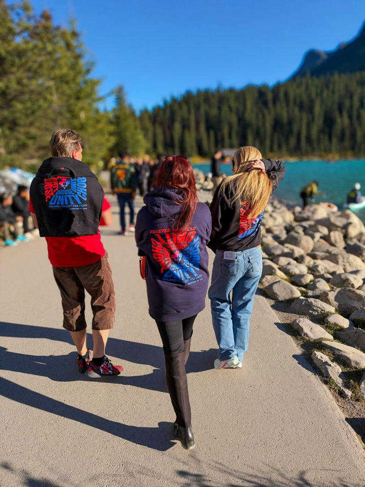 Three people walking by Lake Louise wearing Calgary Concert for Unity hoodies and sweatshirts